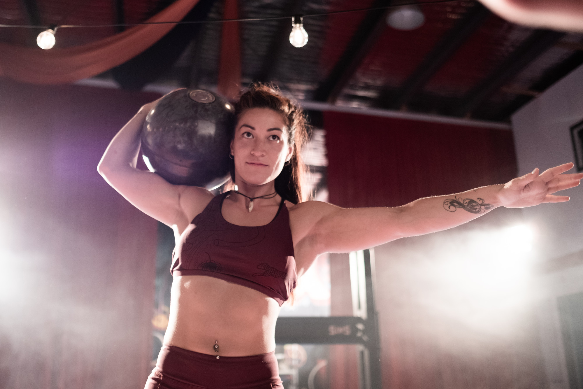 A woman exercising, holding a medicine ball above her shoulder with one hand, the other hand is outstretched.